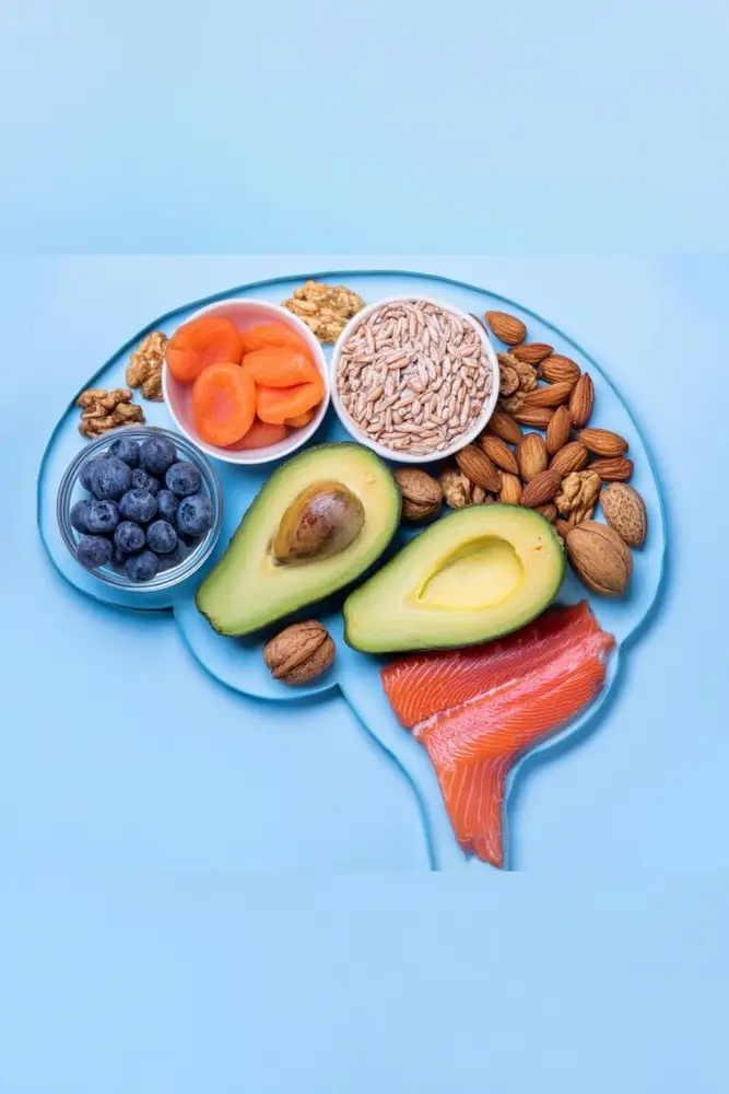 Brain-shaped plate filled with hormone-supporting foods like avocado, salmon, nuts, seeds, blueberries, and dried fruit on a blue background.