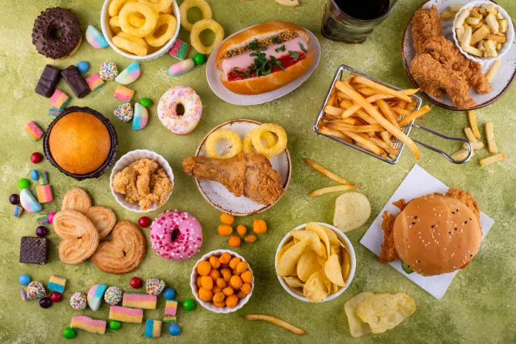 An overhead view of various ultra-processed foods like burgers, fries, donuts, soda, and candy. This image illustrates the types of foods linked to gut health issues and metabolic changes.